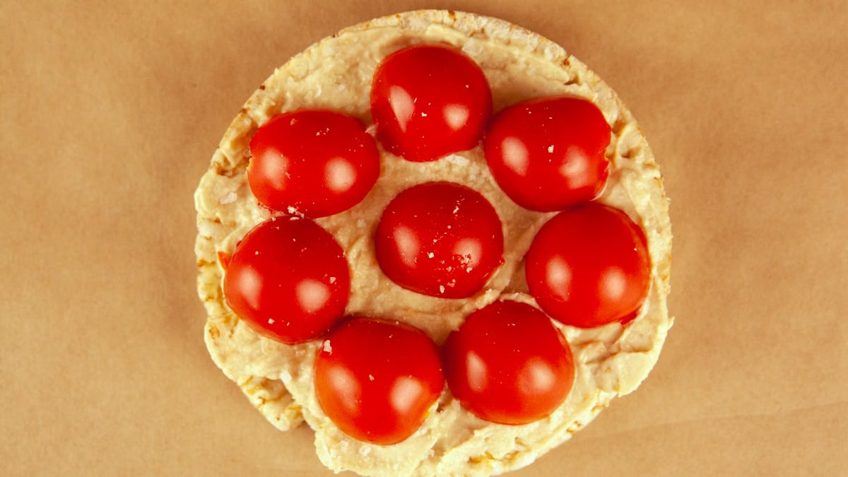 Delicious rice cake topped with hummus and juicy cherry tomatoes.